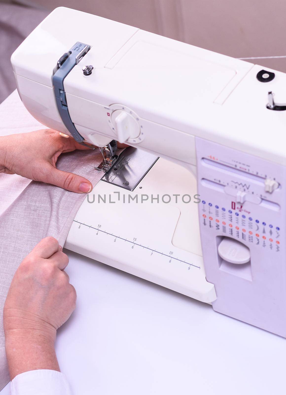 view of sewing process. Top view. Female hands stitching light fabric on machine. Seamstress hands holding textile for linen. Close up. vertical. 