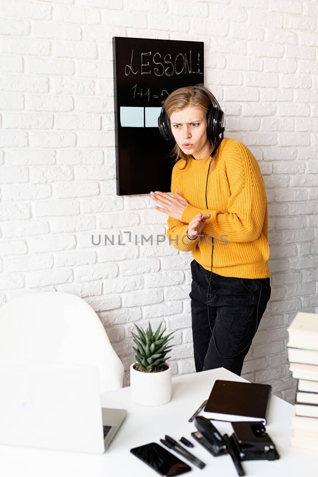 Distance learning. E-learning. Young smiling woman in yellow sweater and black headphones teaching online using video chat on laptop