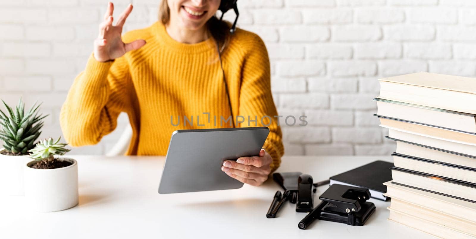 Distance learning. E-learning. Young smiling woman in yellow sweater and black headphones studying online using digital tablet