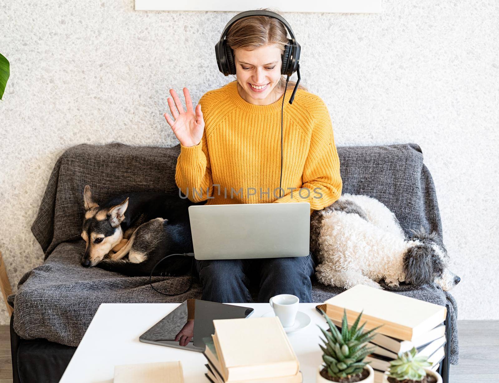 Distance learning. E-learning. Young smiling woman in yellow sweater and black headphones studying online using laptop, sitting on the couch at home