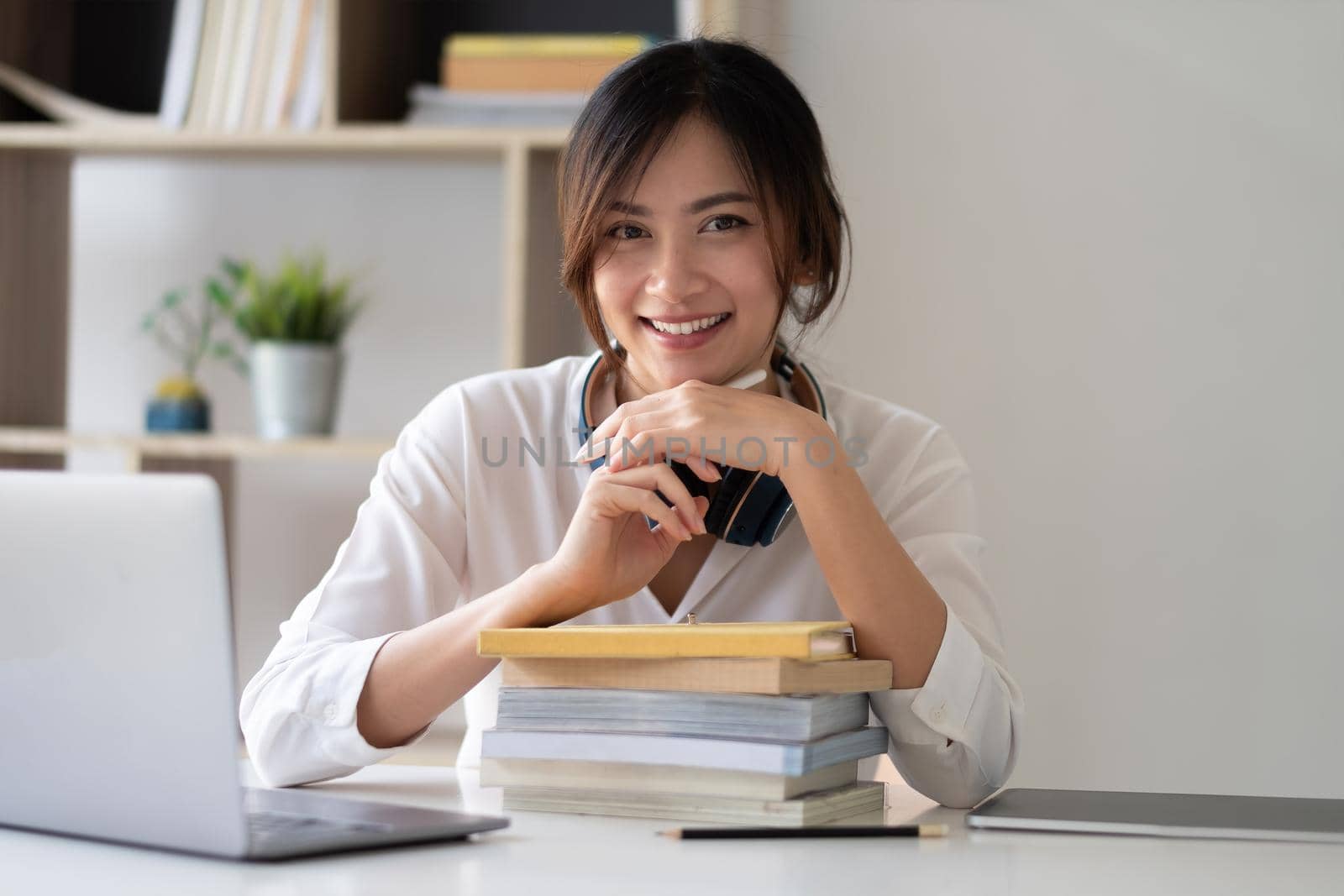 Portrait of happy smiling asian woman sitting at table in room, looking at camera, excited female posing, working at computer, doing homework, preparing report at home. by nateemee