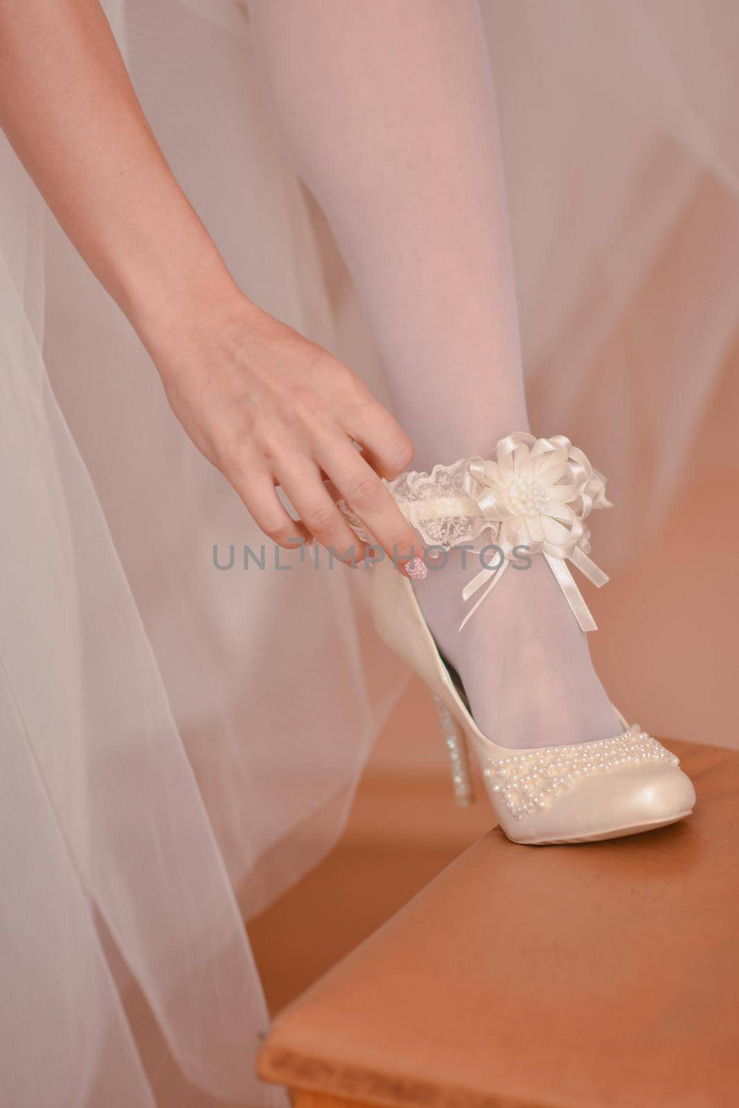 The bride puts a shoe on her foot in the morning before the wedding. Vertical photo