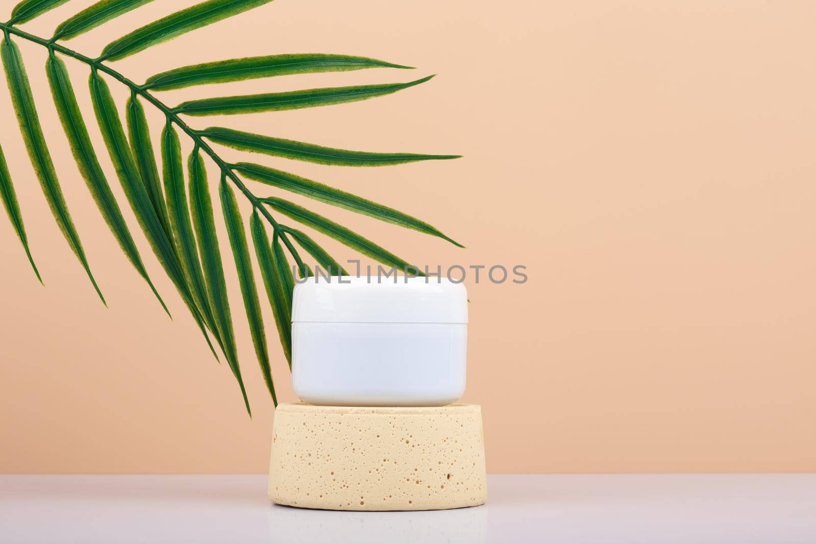 White cream jar with face cream, mask or scrub on podium against beige background with palm leaf and copy space. by Senorina_Irina