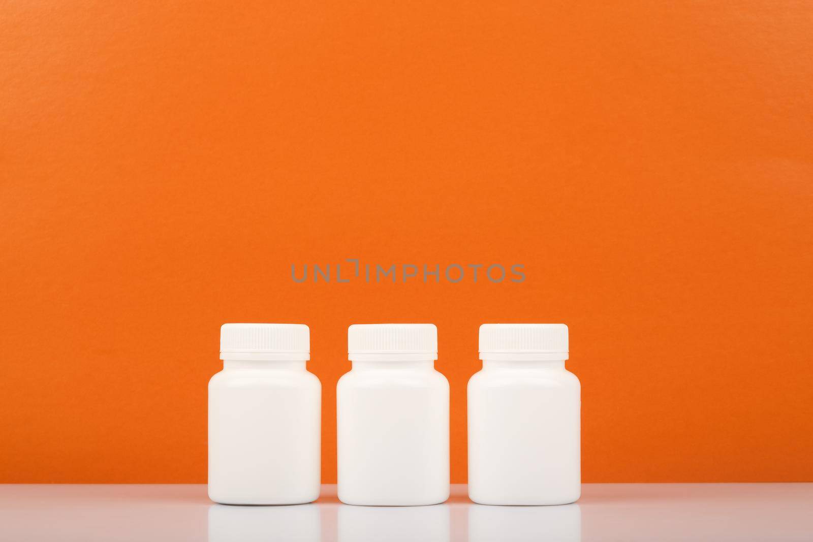 Three white medication bottles in a row against orange background with copy space. Vitamin C concept by Senorina_Irina