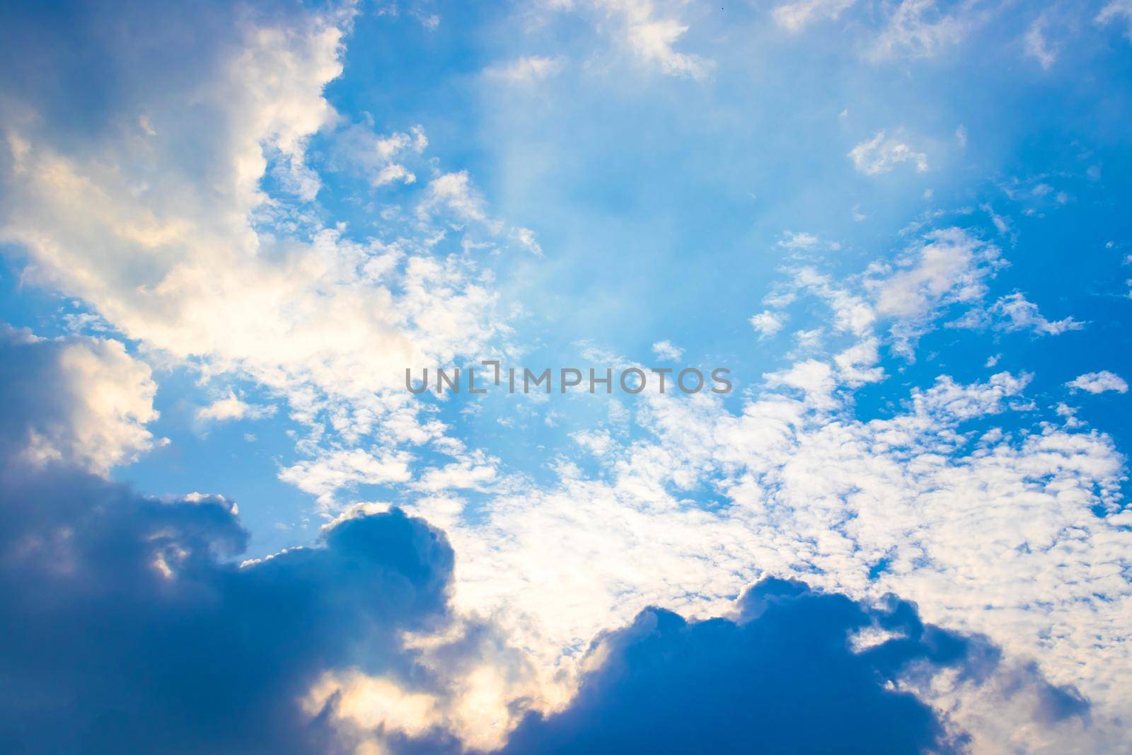 The sun ray behind the clouds in the blue sky.