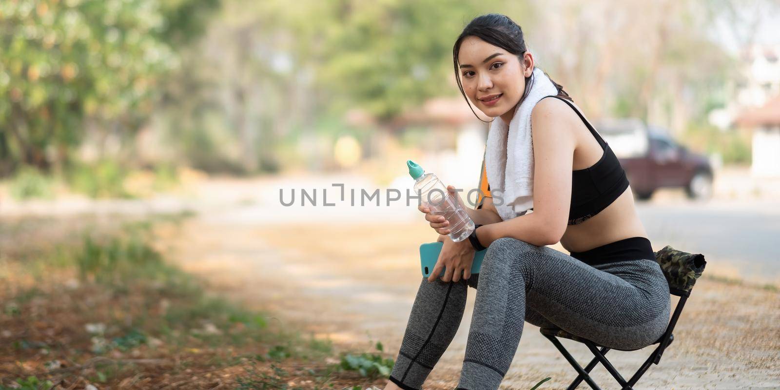 Young athletic woman holding water from a bottle after running in the park by nateemee