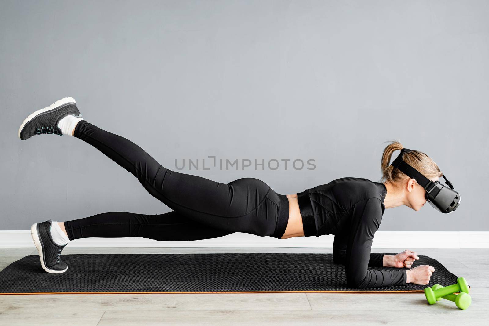 Young blonde woman wearing virtual reality glasses doing plank at home by Desperada