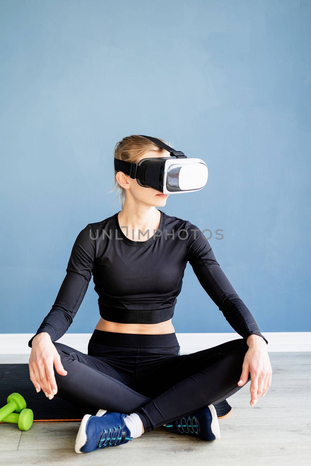 Fitness, sport and technology. Young athletic woman wearing virtual reality glasses sitting on fitness mat
