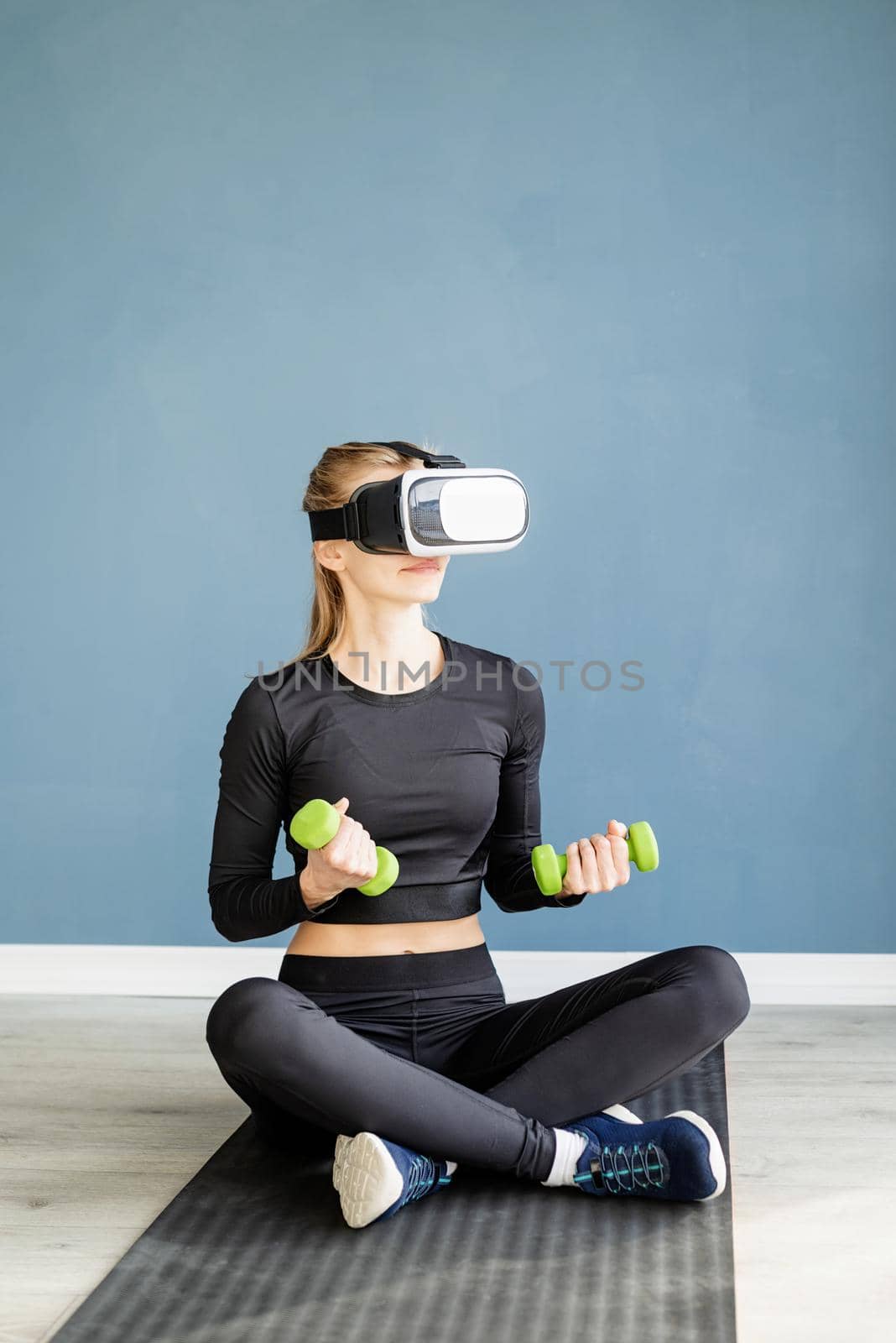 Fitness, sport and technology. Young athletic woman wearing virtual reality glasses sitting on fitness mat