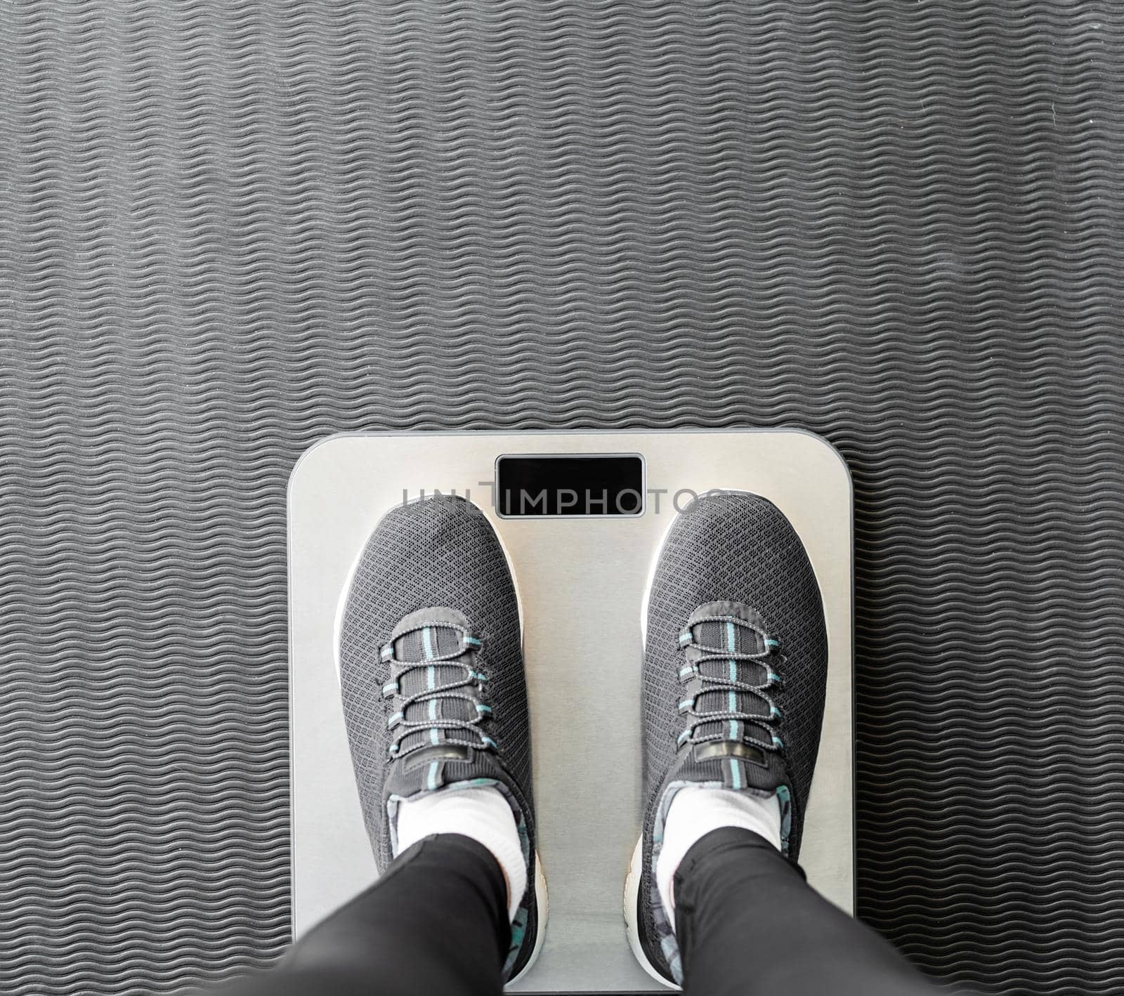 Dieting and weight loss. Top view of female feet in sport shoes standing on scales