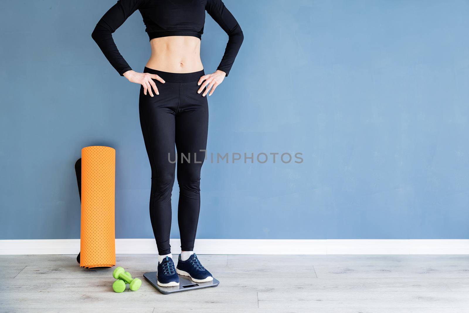 Dieting and weight loss. Woman in black sport clothes standing on scales