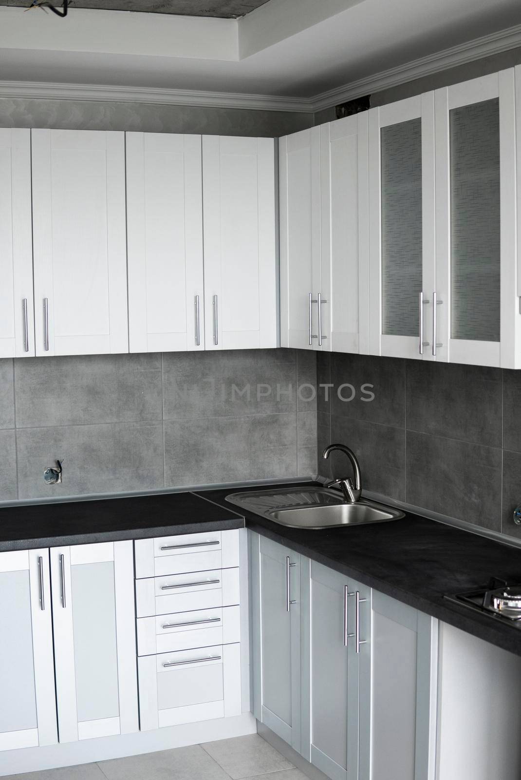 Modern minimalism style kitchen interior in monochrome tones. Custom kitchen with grey white facadesmdf and dark grey countertop with installed kitchen hood and sink. Modular kitchen from chipboard