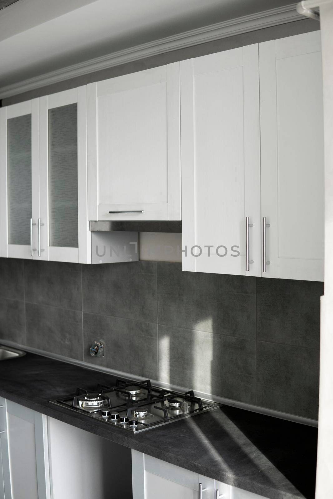 Modern minimalism style kitchen interior in monochrome tones. Custom kitchen with grey white facadesmdf and dark grey countertop with installed kitchen hood and sink. Modular kitchen from chipboard