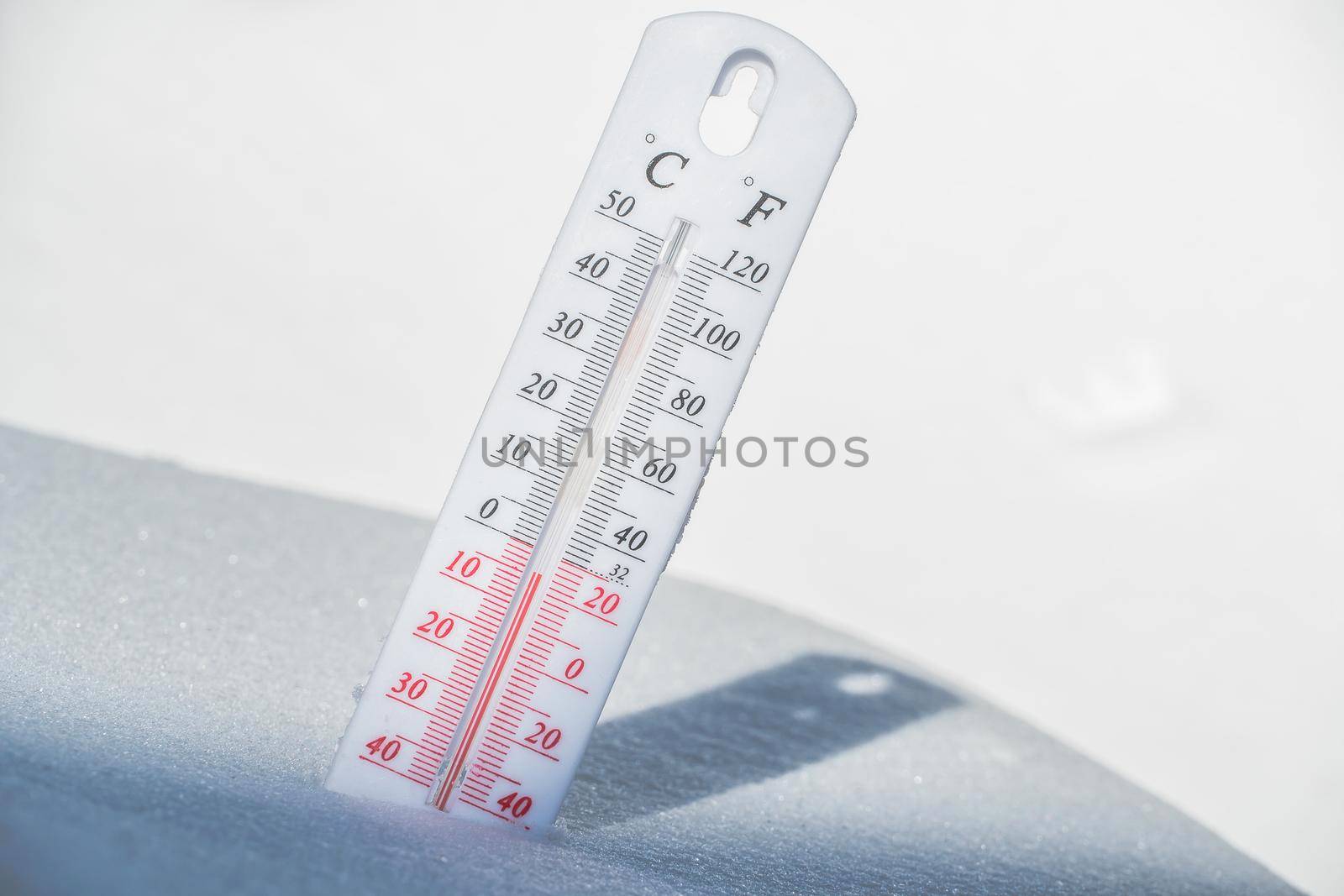 The thermometer lies on the snow and shows a negative temperature in cold weather on the blue sky.Meteorological conditions with low air and ambient temperatures.Climate change and global warming by YevgeniySam