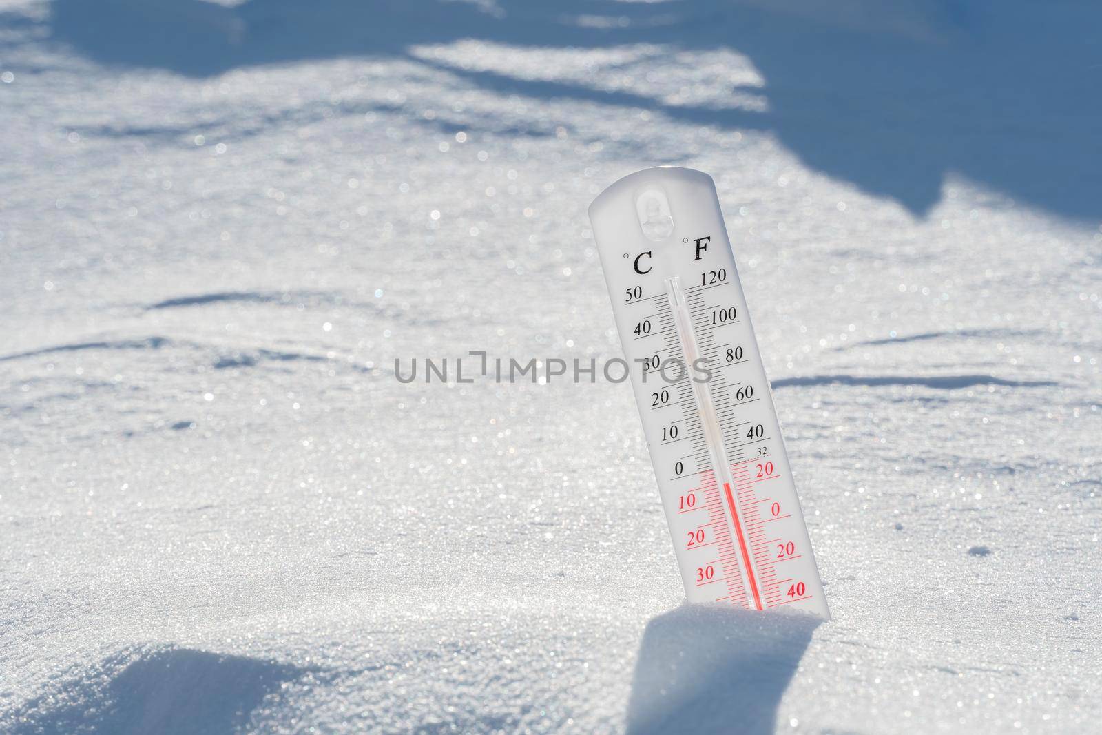 The thermometer lies on the snow and shows a negative temperature in cold weather on the blue sky.Meteorological conditions with low air and ambient temperatures.Climate change and global warming