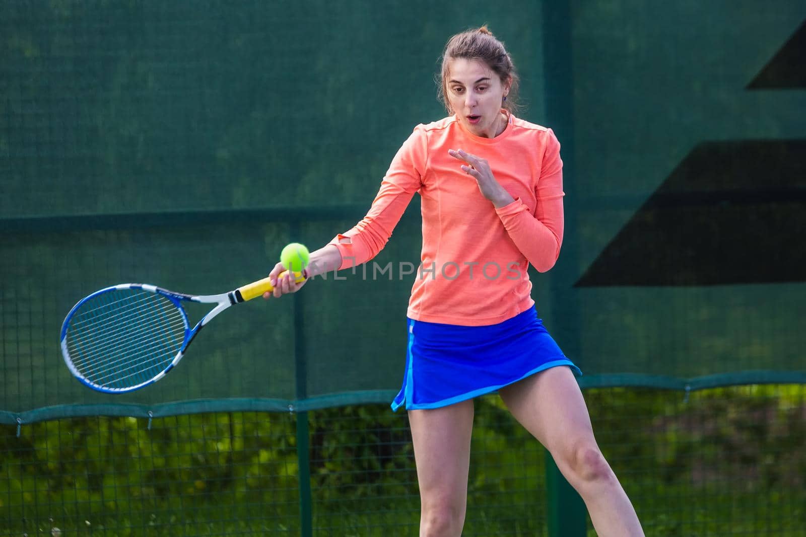 Young woman wearing blue skirt, pink top and tennis shoes during professional tennis match.