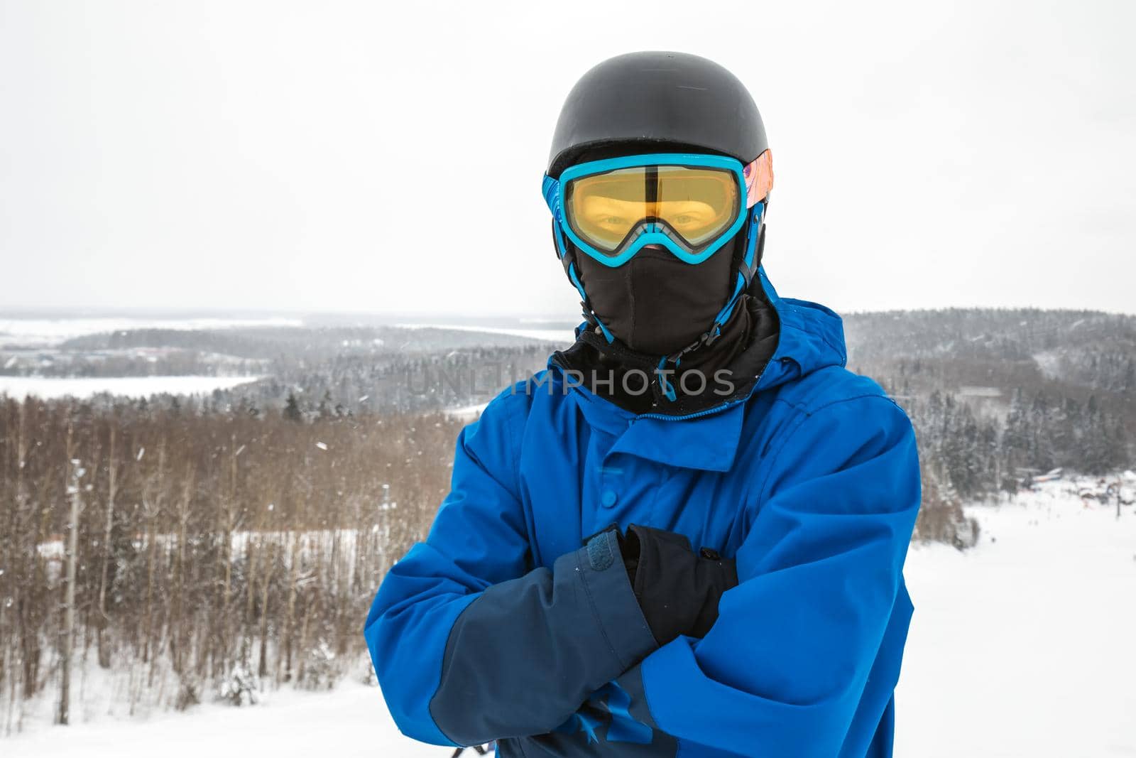 Male in a blue sports suit standing a large snow slope. Snowboarder looking at a camera. Winter forest in the background. Skiing holidays. Close-up. Logoisk, Belarus