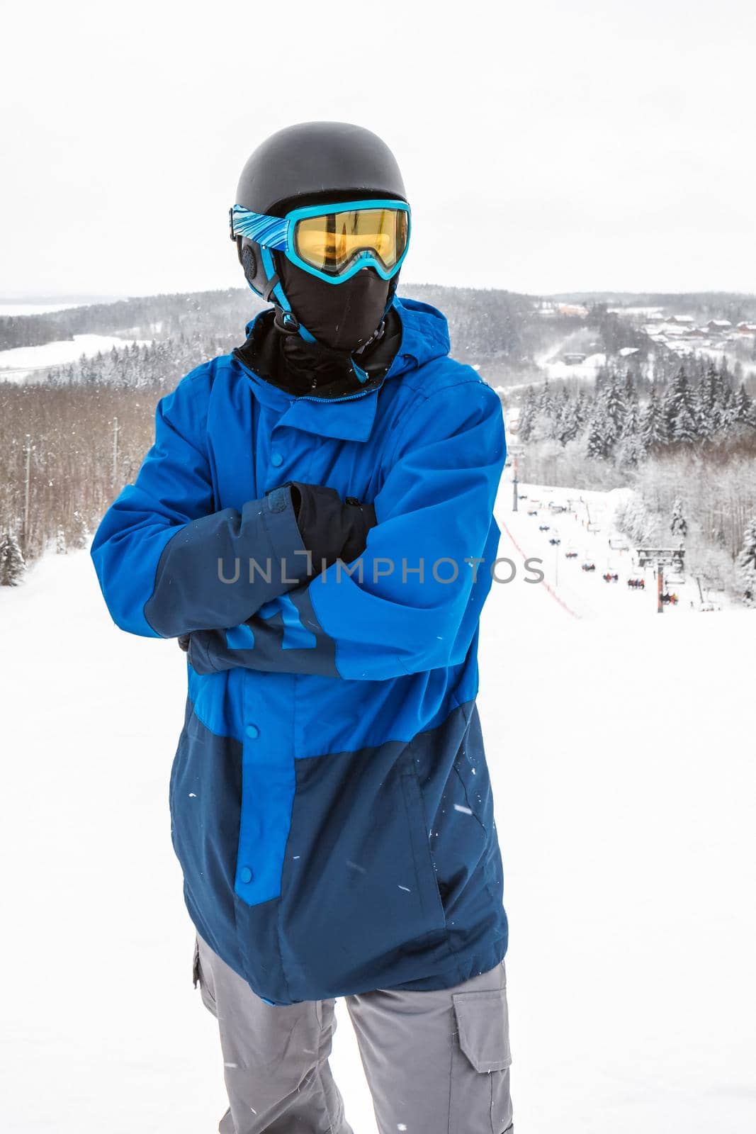 Male in a blue sports suit standing a large snow slope. Snowboarder Snowboarder looks at a beautiful view. Winter forest in the background. Skiing holidays. Close-up. Logoisk, Belarus