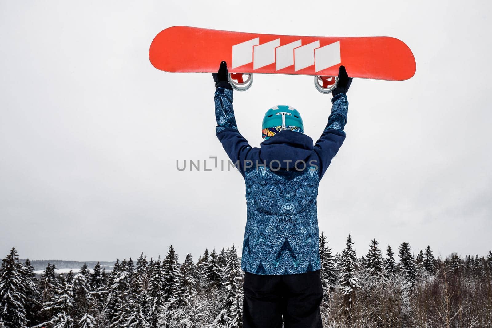 Female in a blue suit standing with a snowboard on a large snow slope. Snowboarder holds the snowboard over his head. Skiing holidays. Logoisk, Belarus