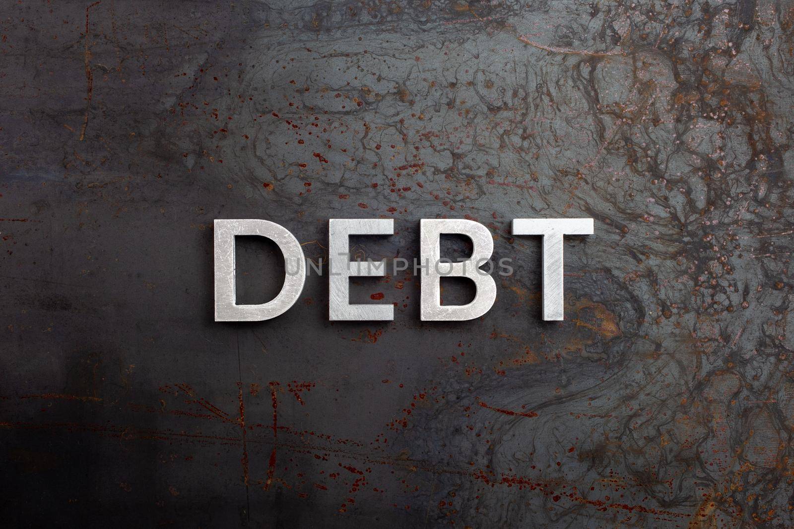 the word debt laid with silver letters on raw rusted steel sheet surface in flat lay perspective.