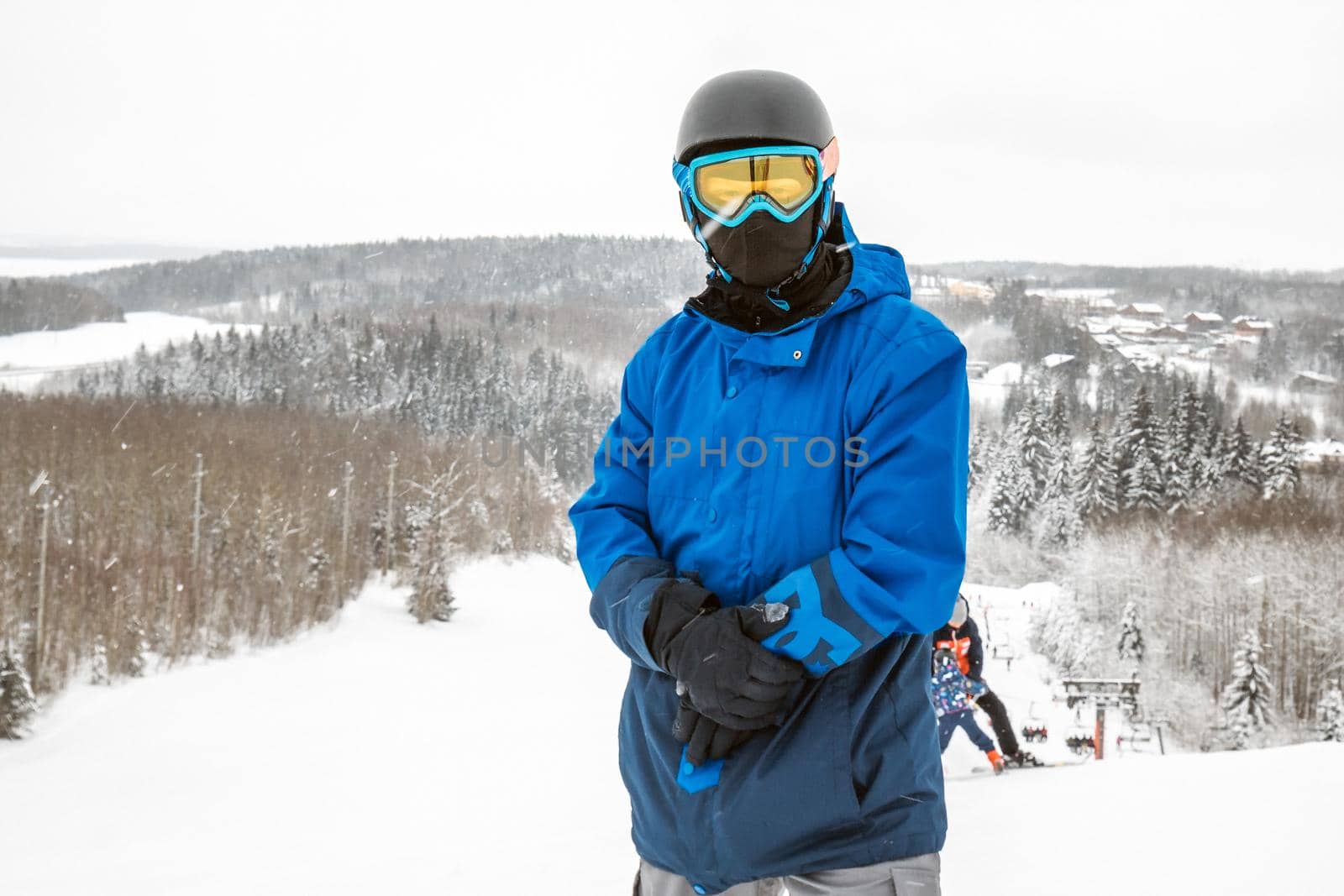 Male in a blue sports suit standing a large snow slope. Snowboarder looking at a camera. Winter forest in the background. Skiing holidays. Close-up. Logoisk, Belarus