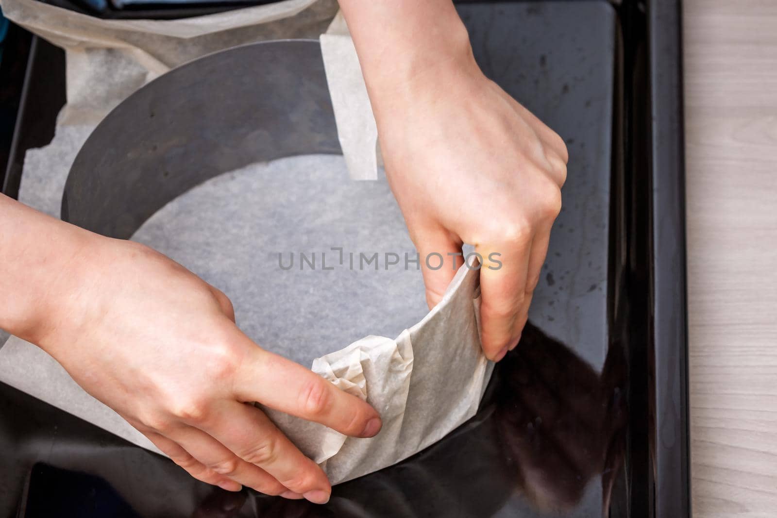 Hands hold iron cake form on baking paper on a tray. Preparing homemade cake.