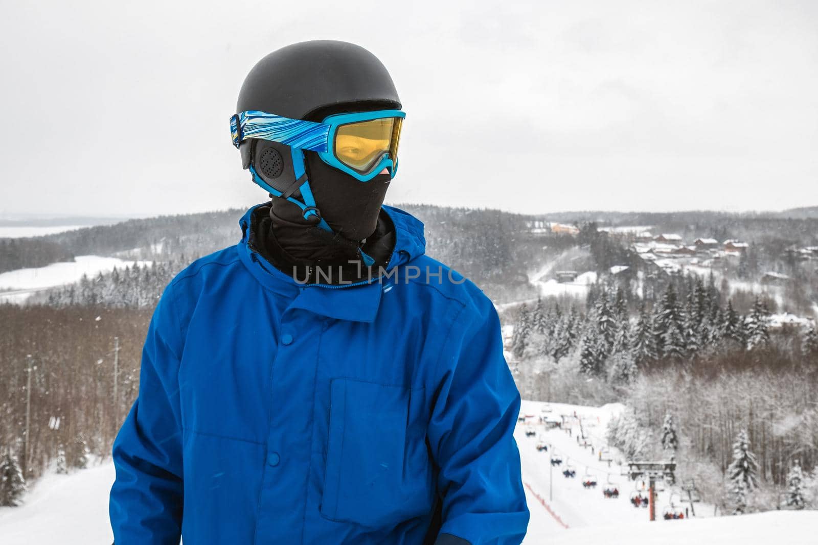 Male in a blue sports suit standing a large snow slope. Snowboarder Snowboarder looks at a beautiful view. Winter forest in the background. Skiing holidays. Close-up. Logoisk, Belarus