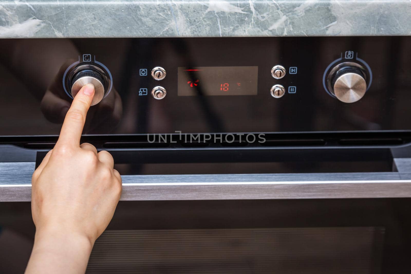 Female hand turning on the oven to make a cake at home. Close-up of the oven knob. View of the black electric oven, knob with a hot air icon. The concept of heating food, baking a cake.