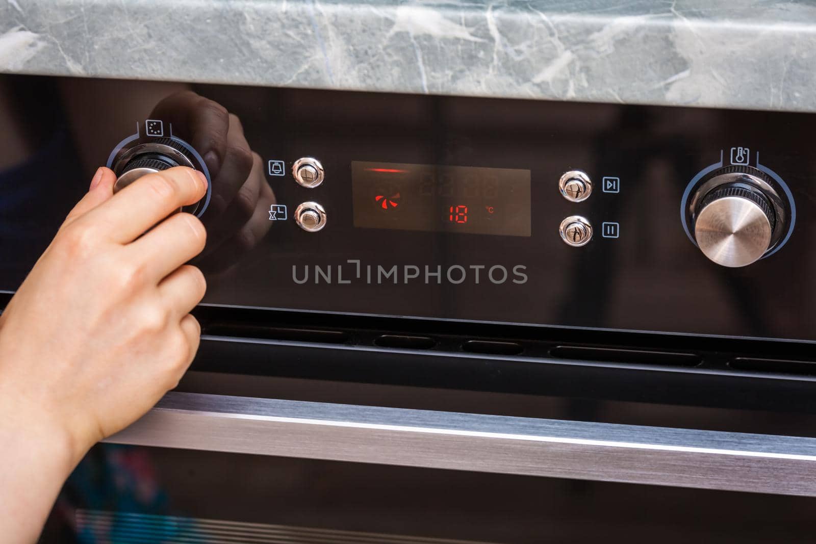 Female hand turning on the oven to make a cake at home. Close-up of the oven knob. View of the black electric oven, knob with a hot air icon. The concept of heating food, baking a cake.