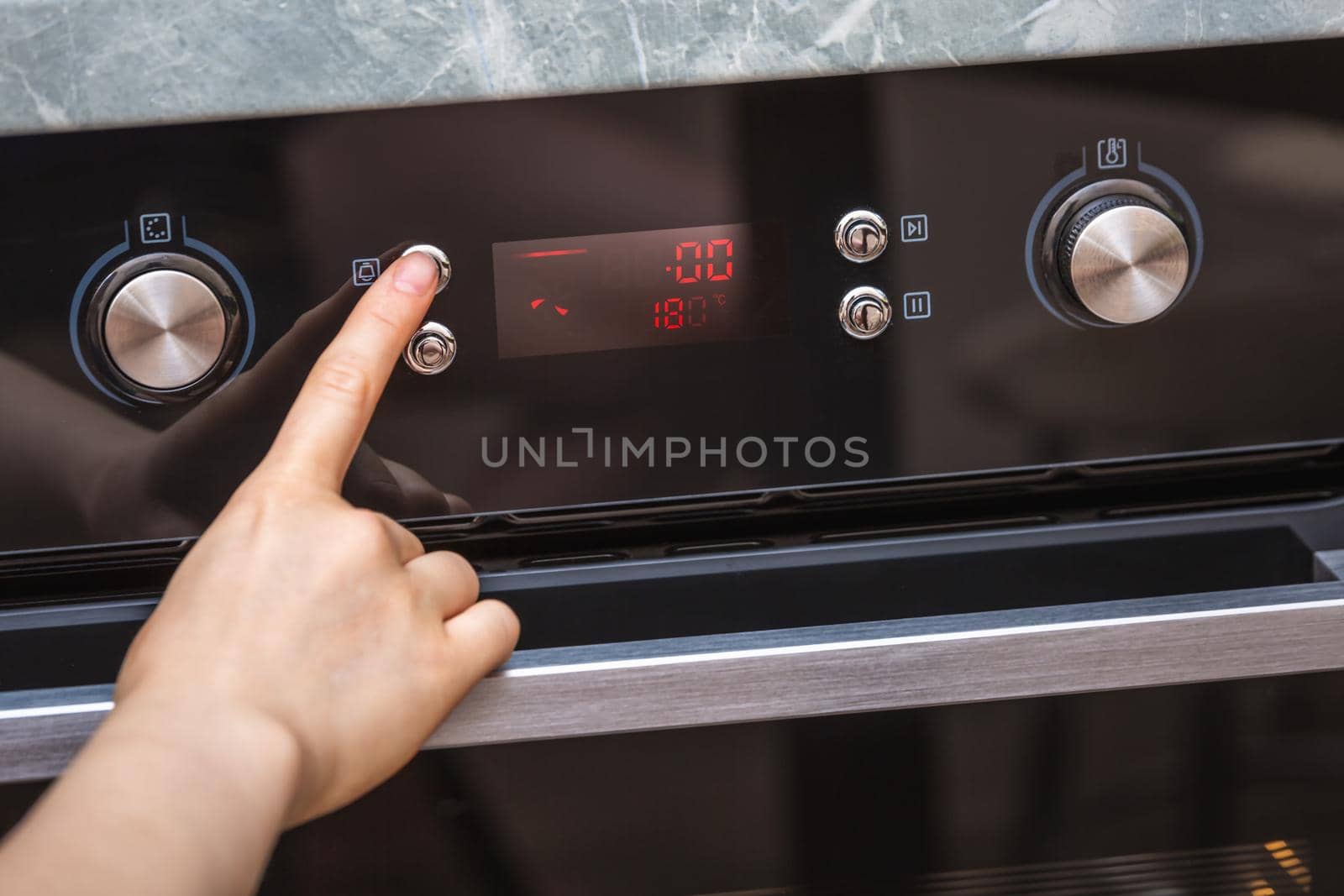 Female hand turning on the oven to make a cake at home. Close-up of the oven knob. View of the black electric oven, knob with a hot air icon. The concept of heating food, baking a cake.