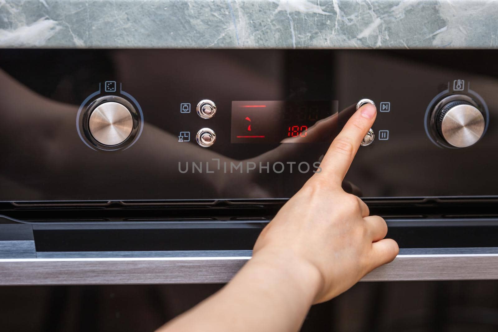 Female hand turning on the oven to make a cake at home. Close-up of the oven knob. View of the black electric oven, knob with a hot air icon. The concept of heating food, baking a cake.