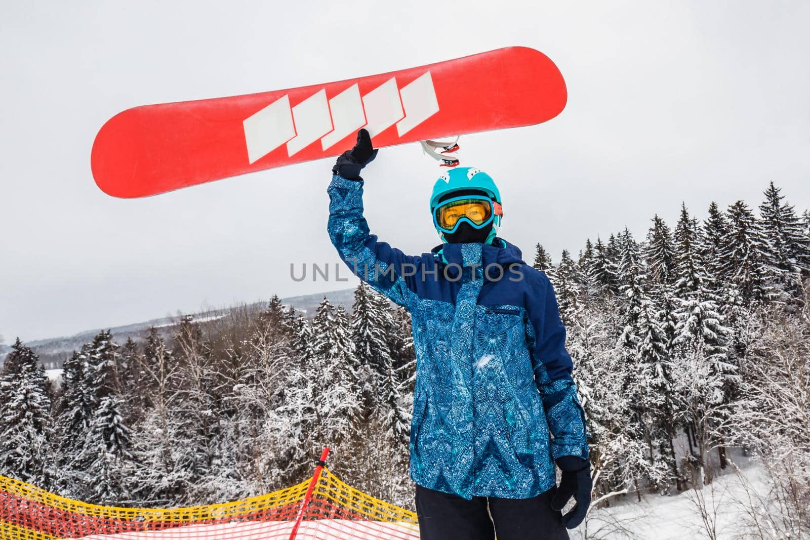 Female in a blue suit standing with a snowboard on a large snow slope. Snowboarder holds the snowboard over his head. Skiing holidays. Logoisk, Belarus