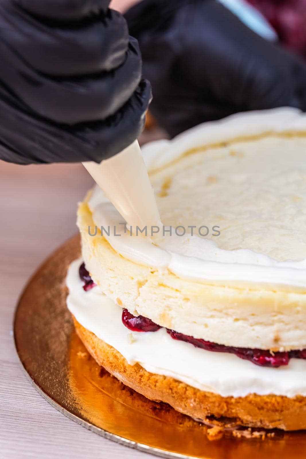 Female hand in black glove squeezes out cream on a cheesecake with coconut.