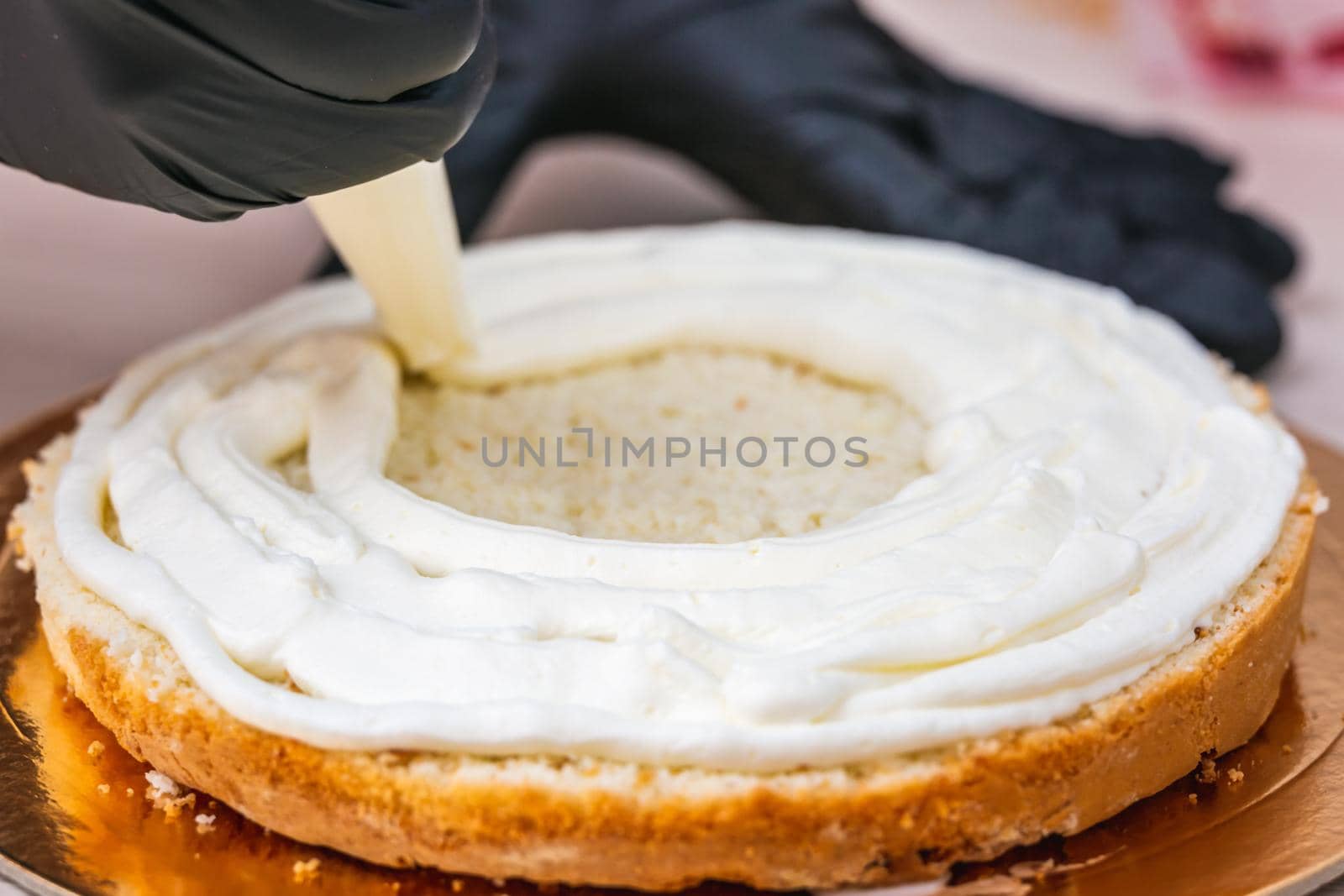 Female hand in black glove squeezes out cream on a cheesecake with coconut.