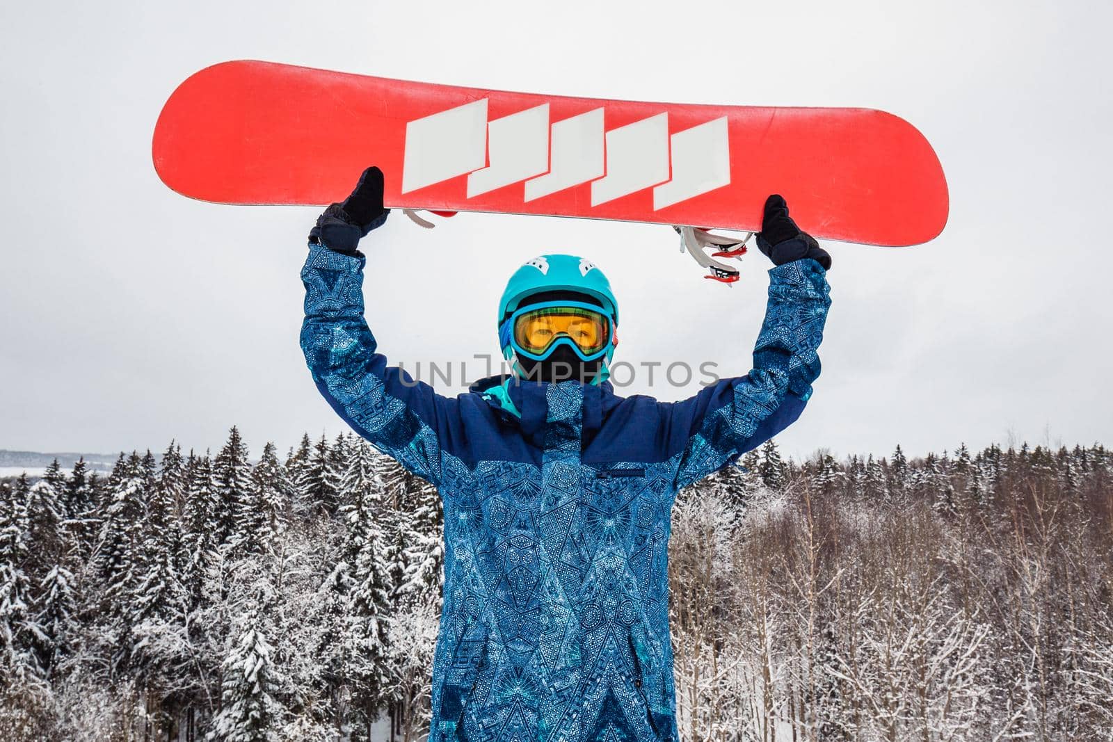 Female in a blue suit standing with a snowboard on a large snow slope. Snowboarder holds the snowboard over his head. Skiing holidays. Logoisk, Belarus