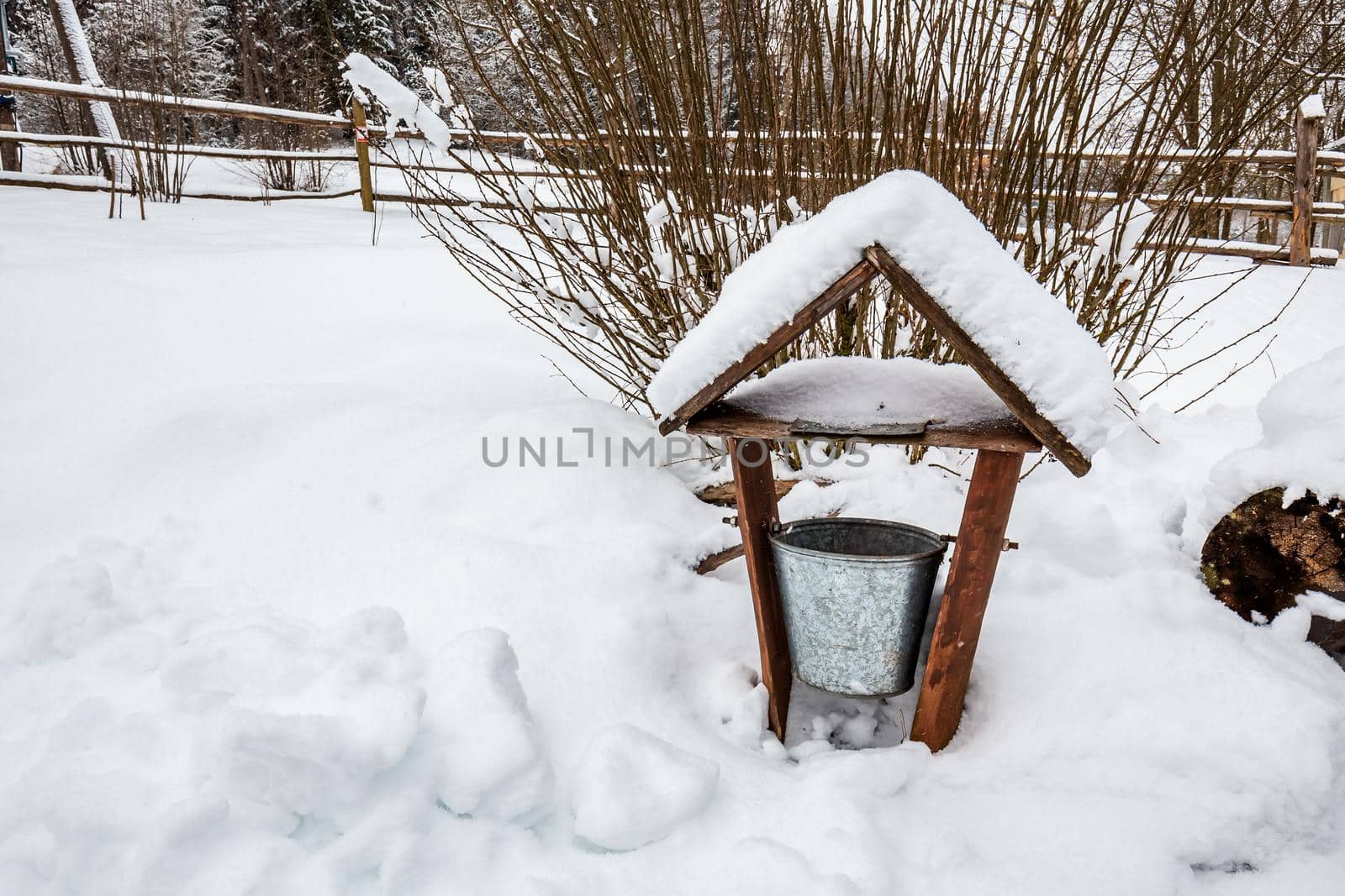 Decorated wooden house with textured wall and bucket covered with a heavy snow in the village in Belarus.