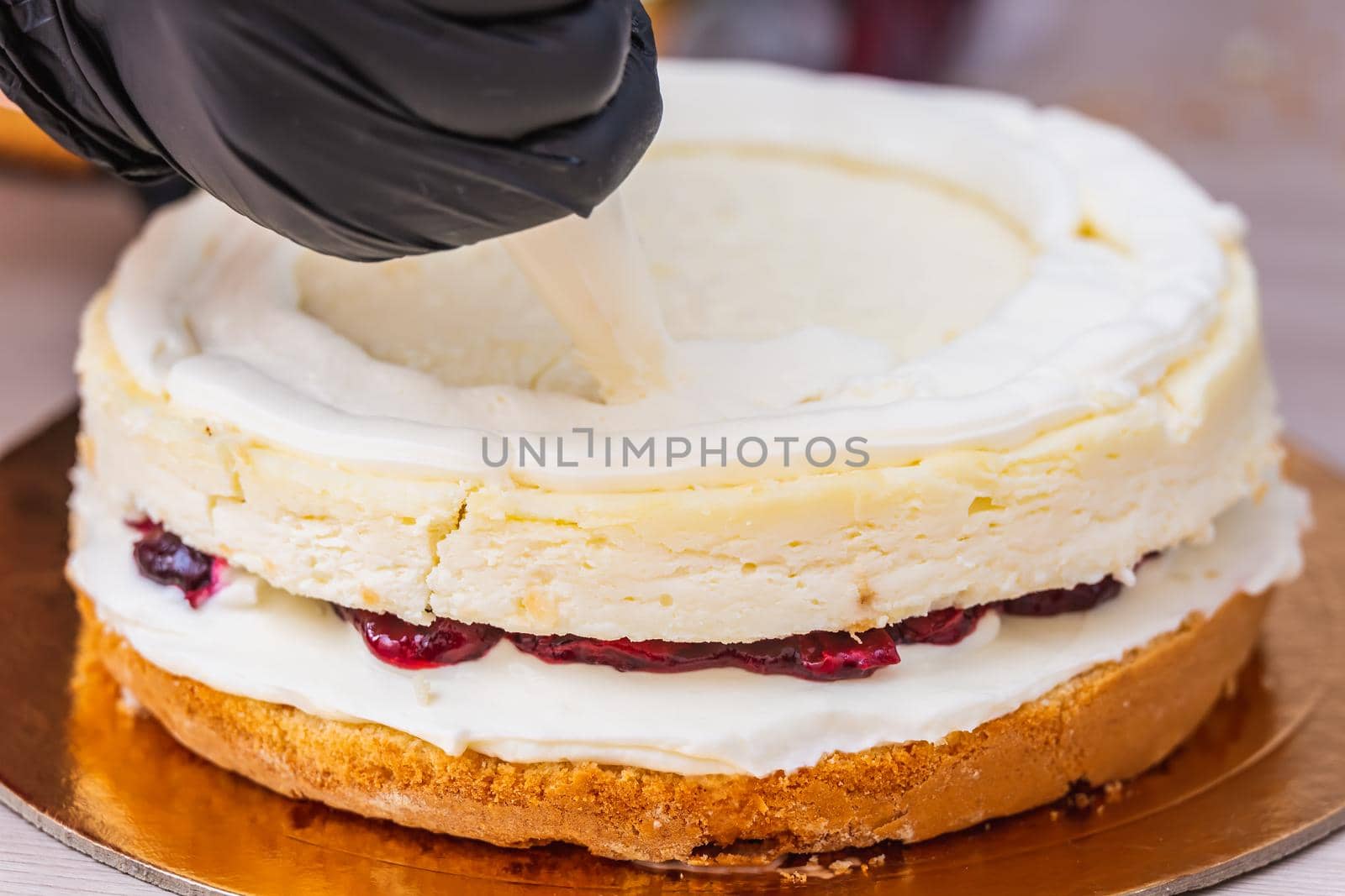 Female hand in black glove squeezes out cream on a cheesecake with coconut.