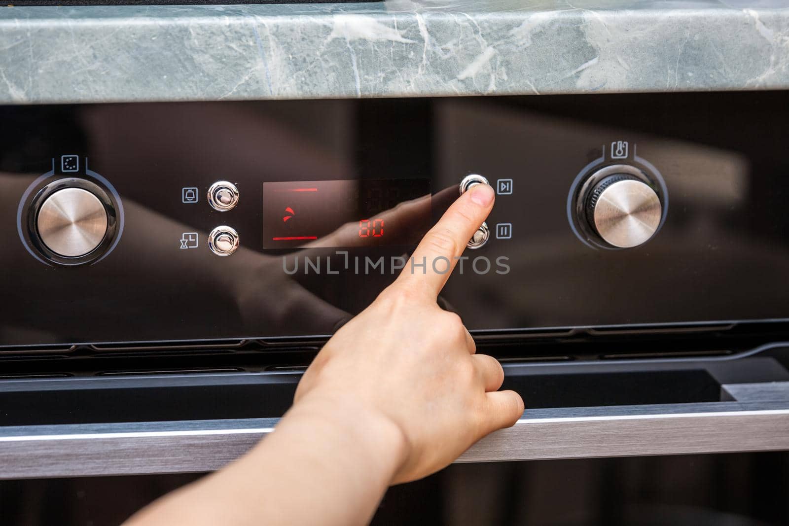 Female hand turning on the oven to make a cake at home. Close-up of the oven knob. View of the black electric oven, knob with a hot air icon. The concept of heating food, baking a cake.