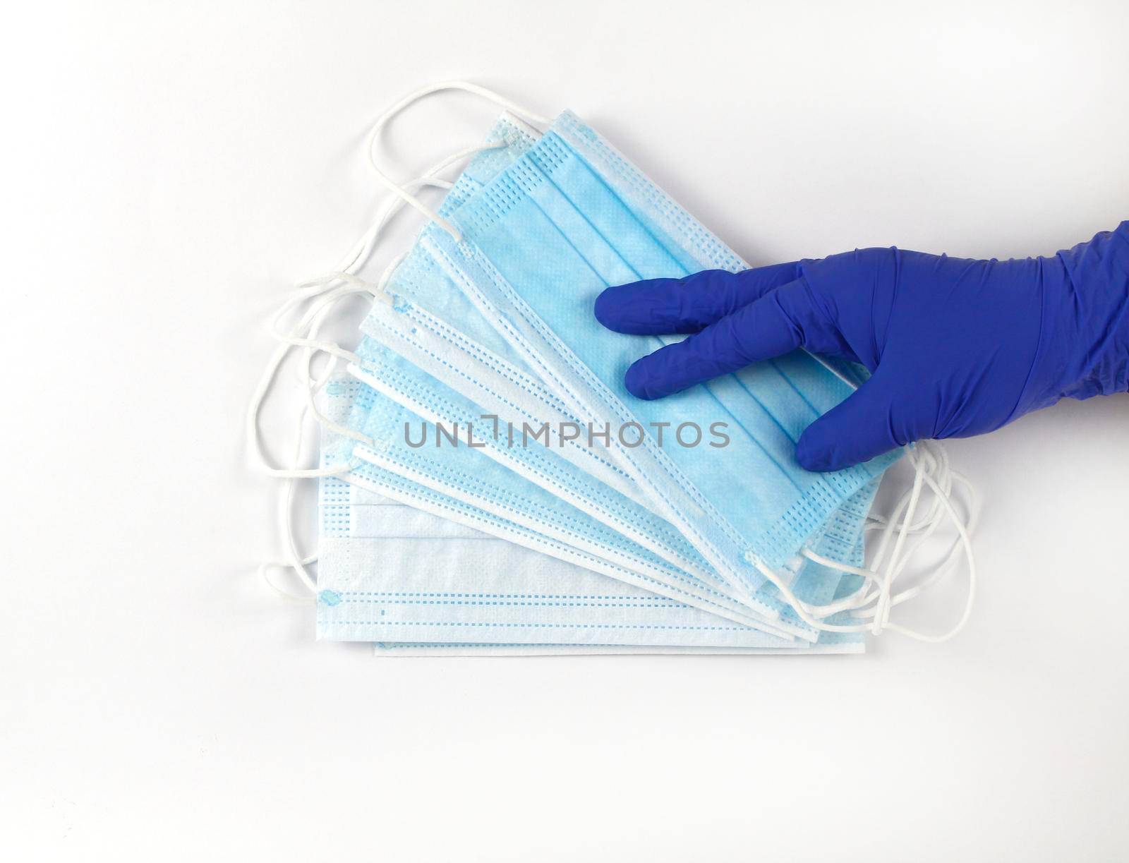 Hand on blue surgical gloves hanging Disposable Medical masks on white background. Covid-19 and healthcare concept