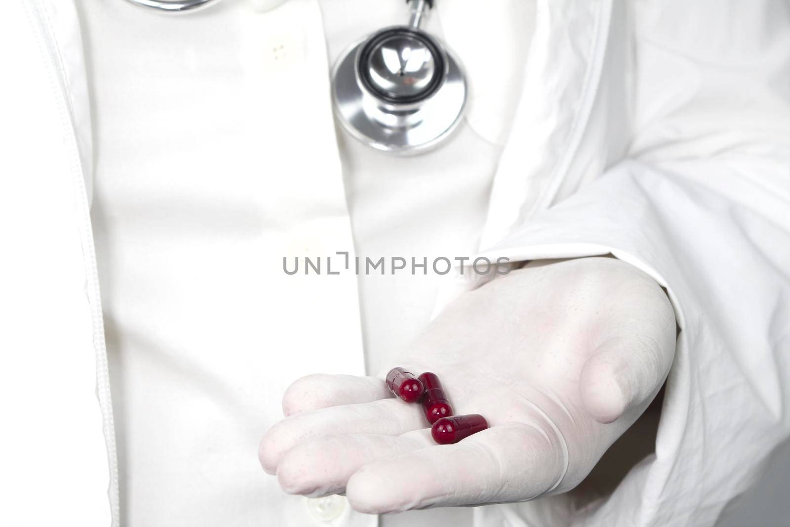 Doctor in white surgical gloves and wearing stethoscope holding red capsules