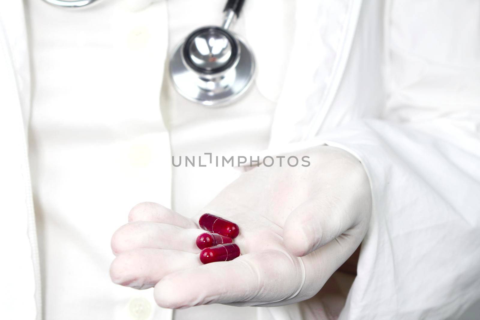 Doctor in white surgical gloves and wearing stethoscope holding red capsules