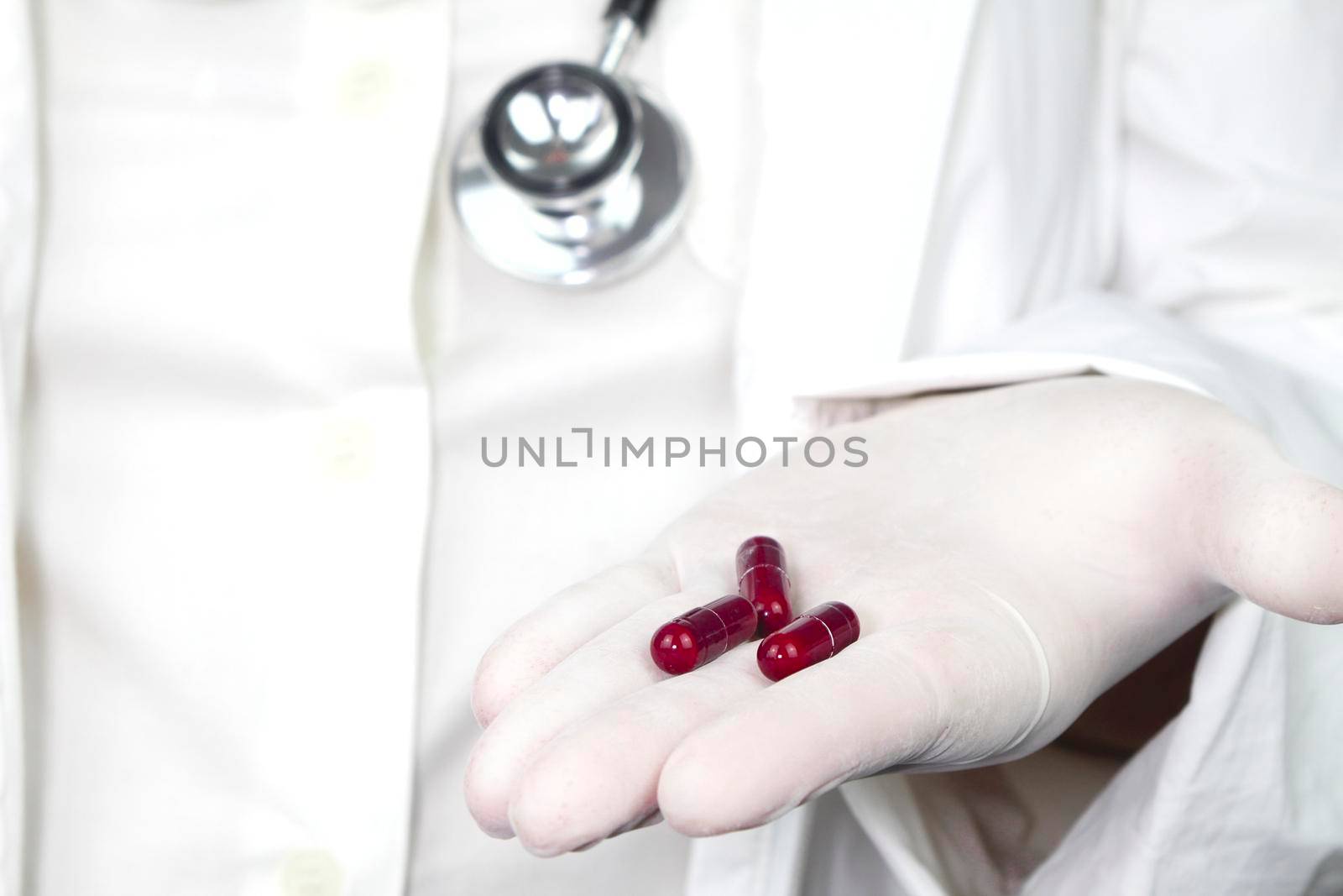 Doctor in white surgical gloves and wearing stethoscope holding red capsules