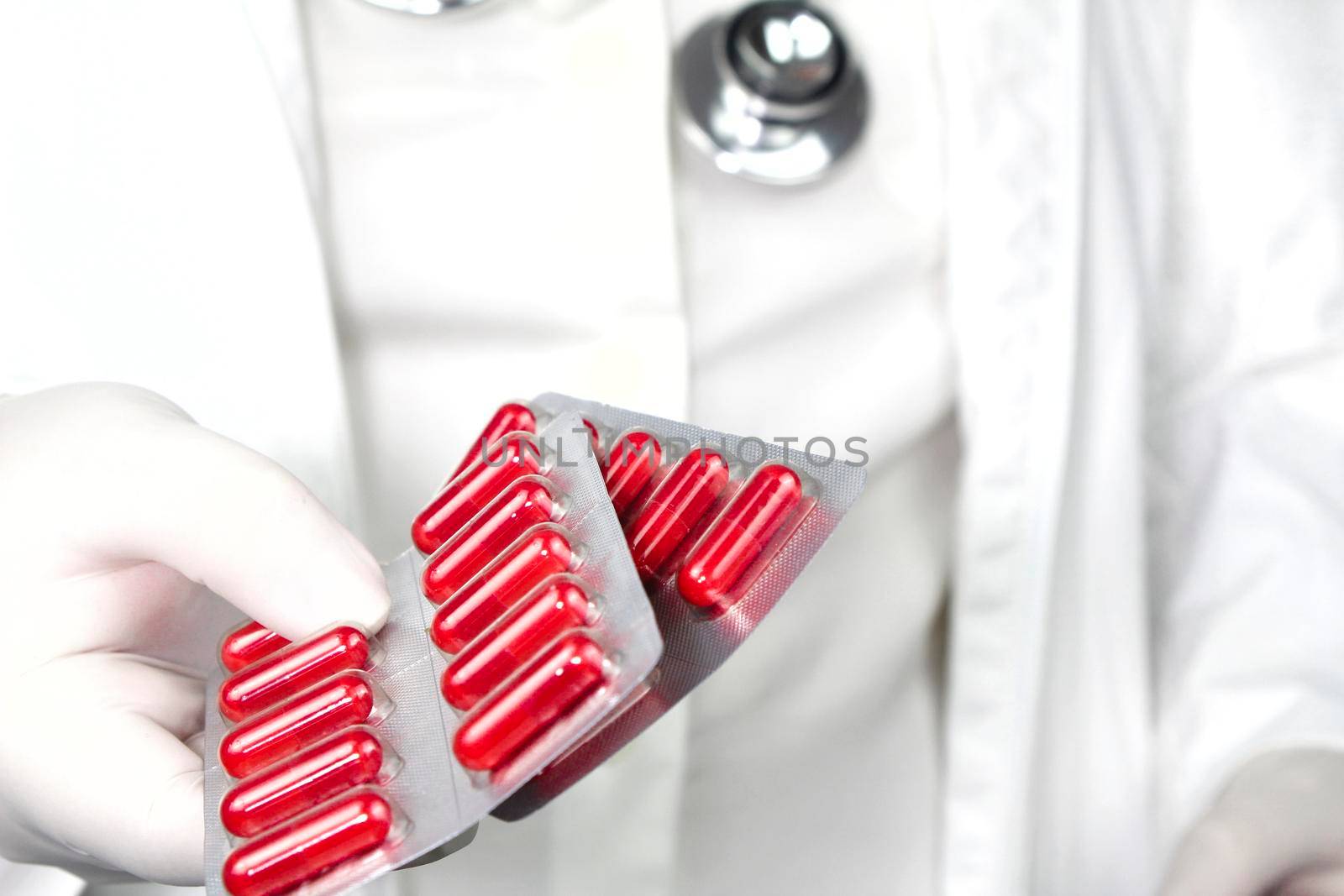 Doctor in white surgical gloves and wearing stethoscope holding red capsule blisters