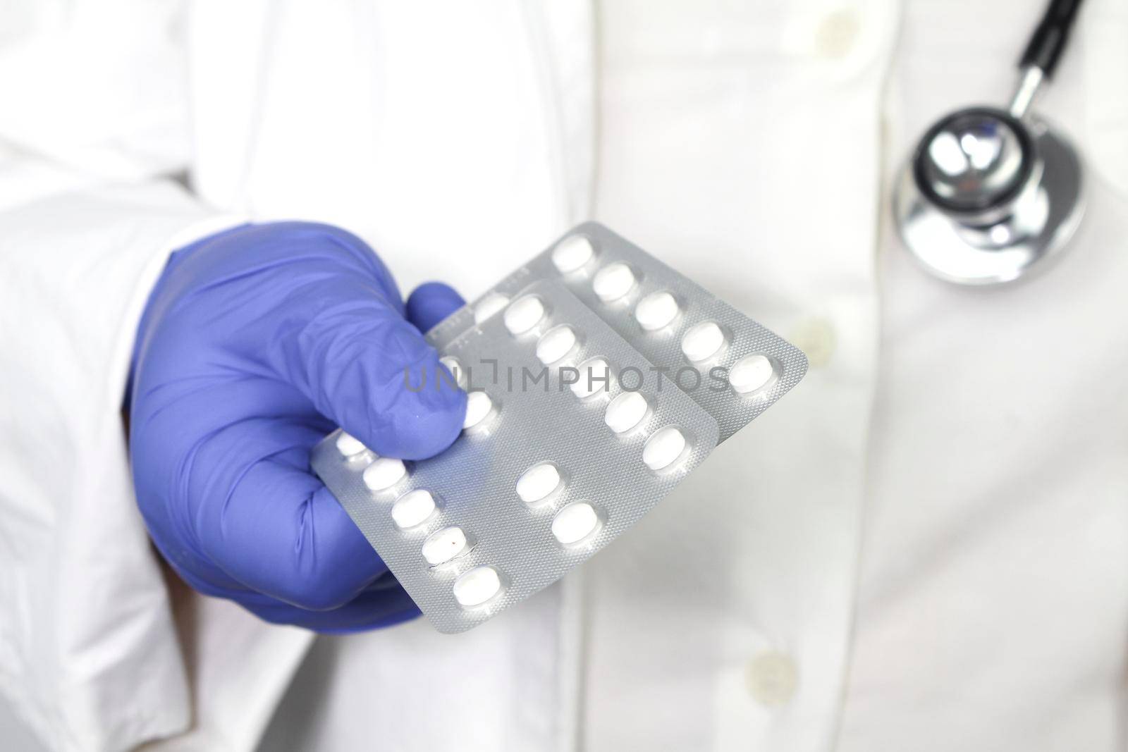 Doctor in blue surgical gloves and wearing stethoscope holding pill blisters