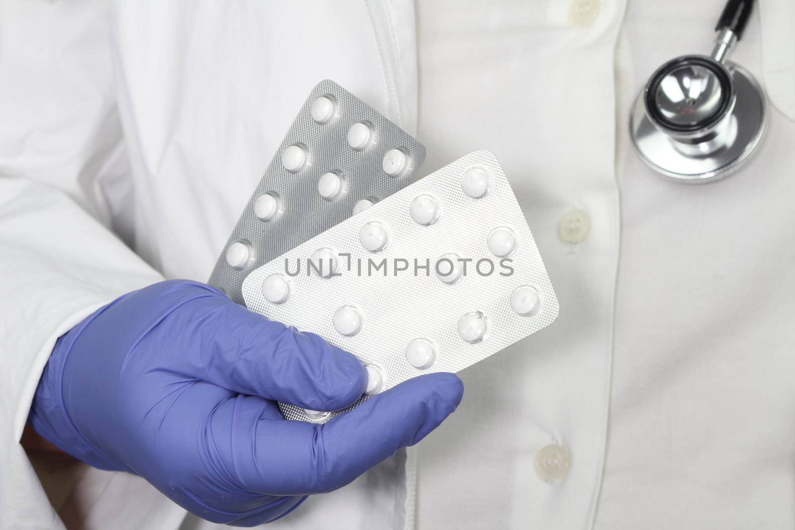 Doctor in blue surgical gloves and wearing stethoscope holding pill blisters