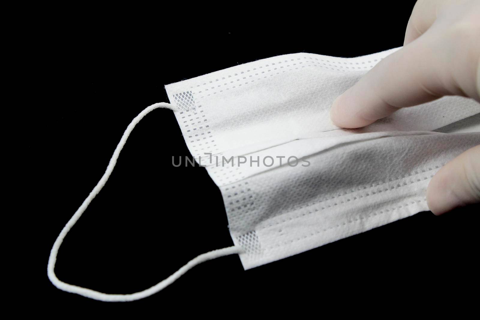 Hand on surgical gloves hanging Disposable Medical mask on black background. Covid-19 and healthcare concept