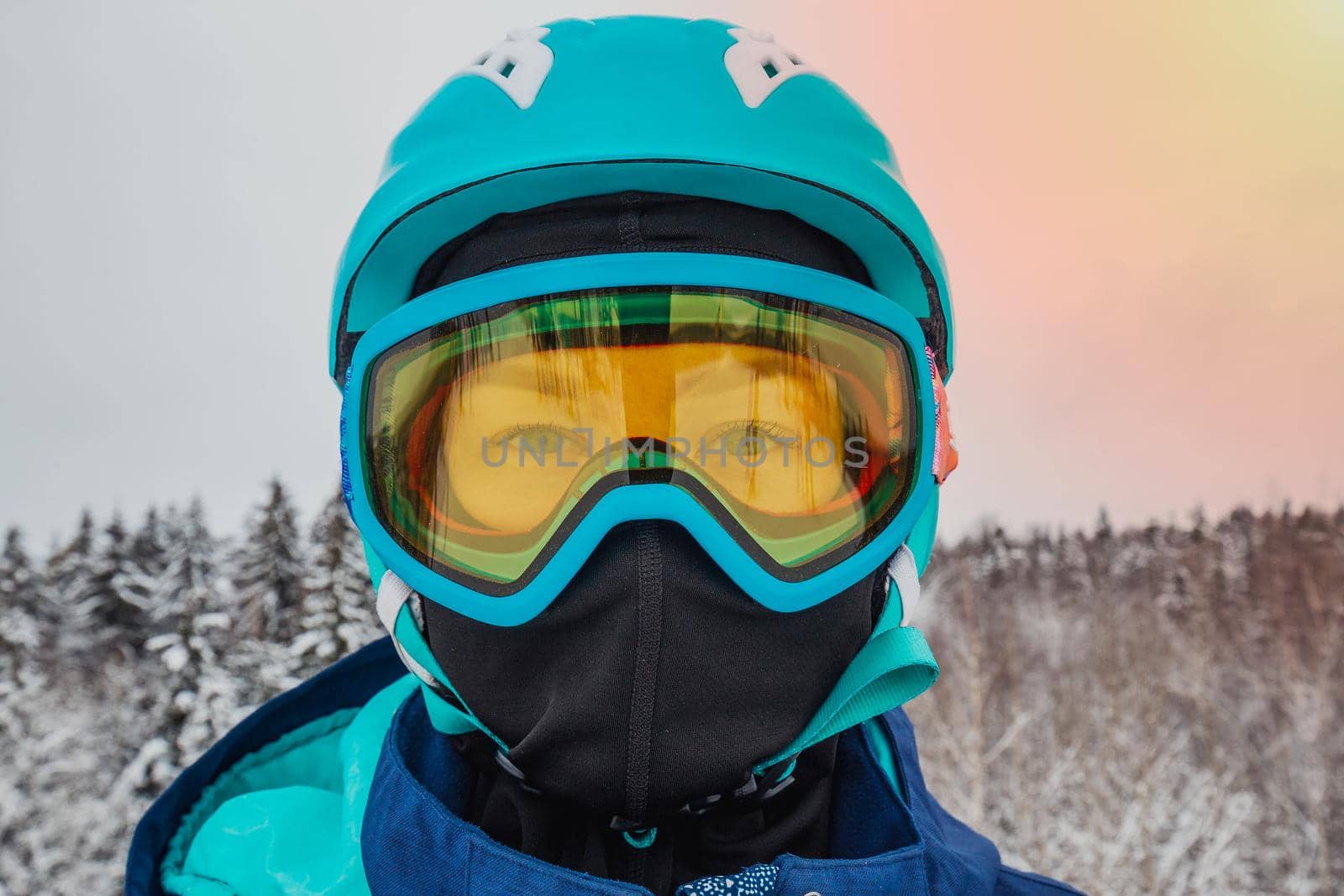 Female in ski mask with blue eyes. Snowboarder looking at camera. Behind there is a beautiful view of the snow-covered forest. Ski vacation. Logoisk, Belarus