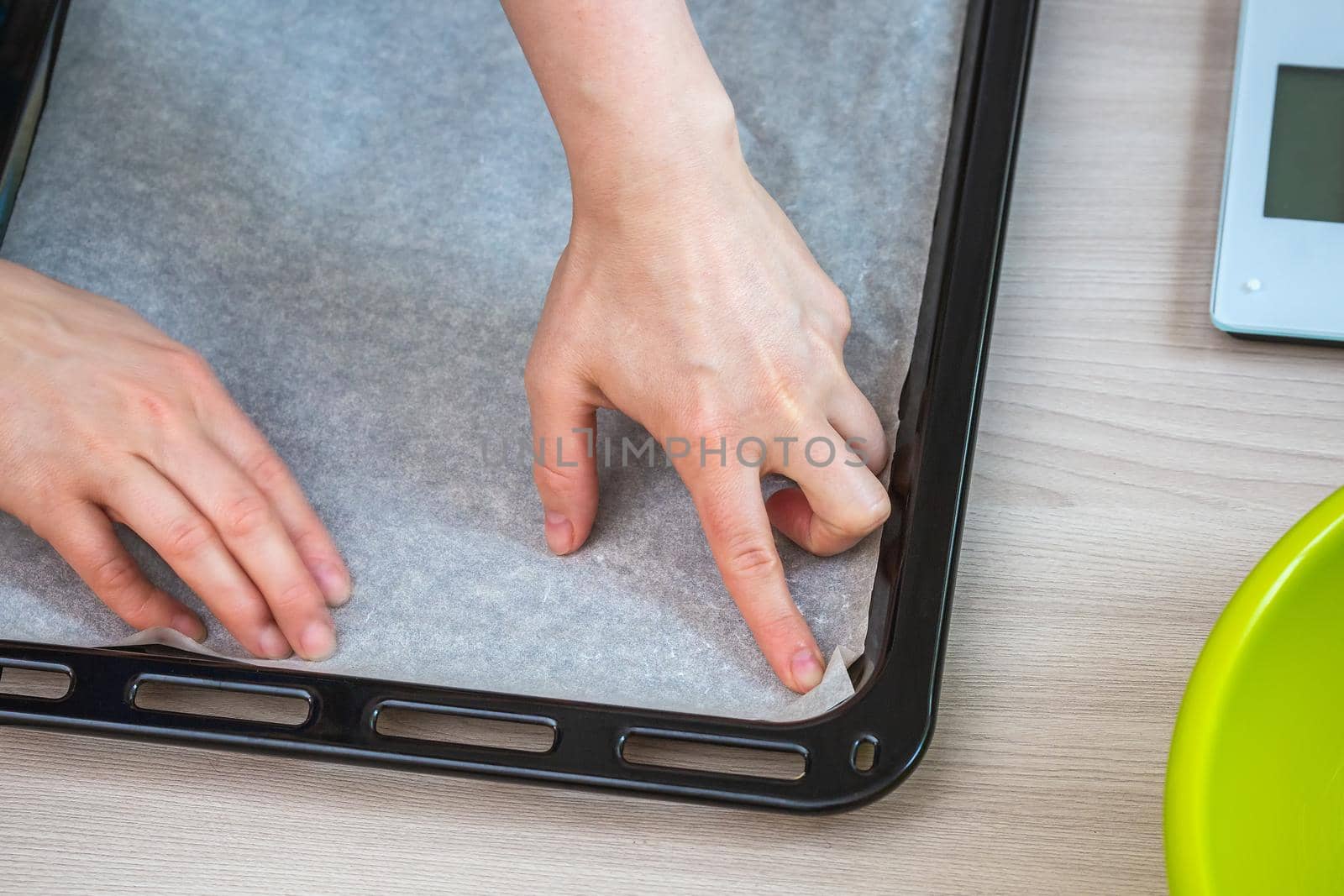Hands hold baking paper on a tray. Preparing homemade cake.