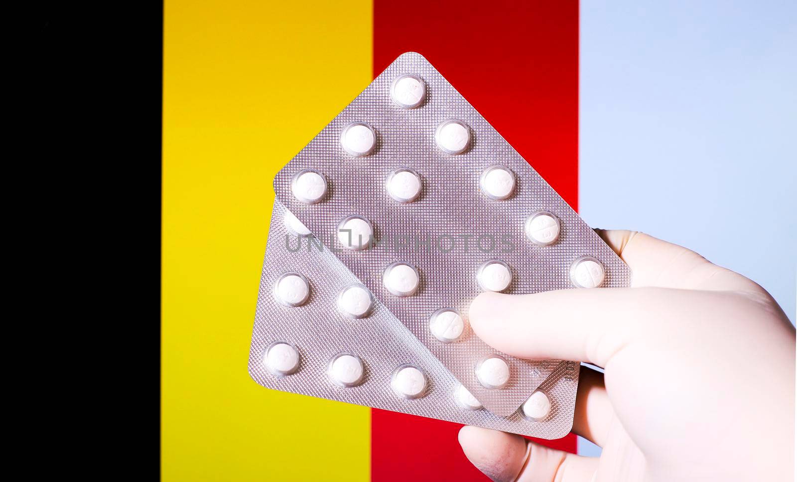 Hand in surgical glove holding pill blisters. Belgian flag in the background