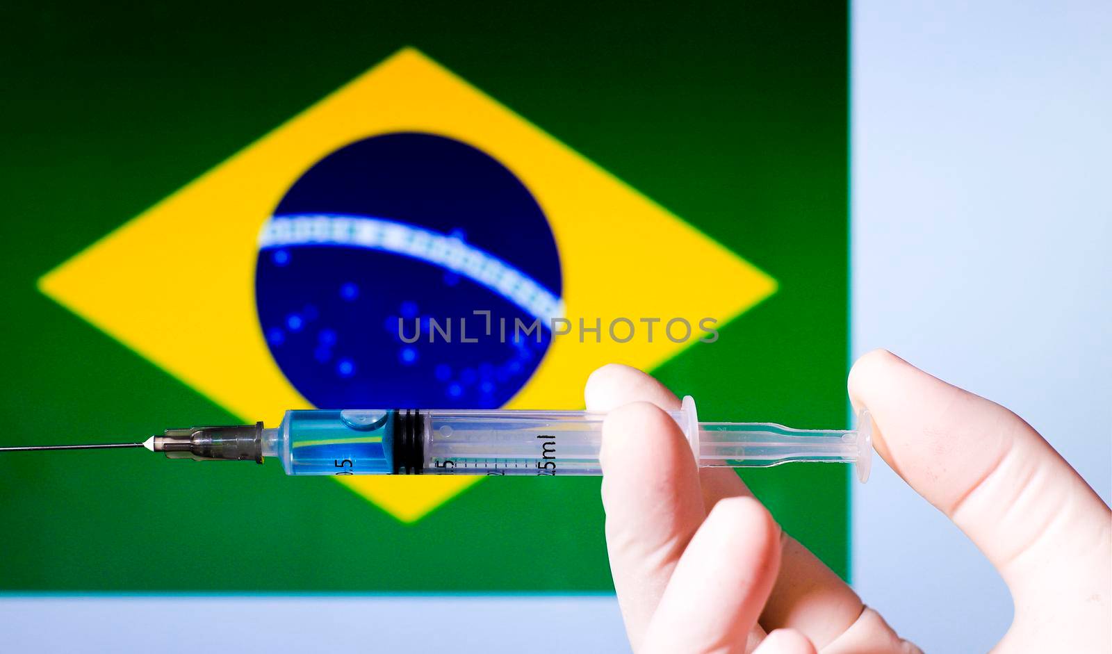 Hand in surgery glove holding syringe with covid vaccine. Brazilian flag in the background